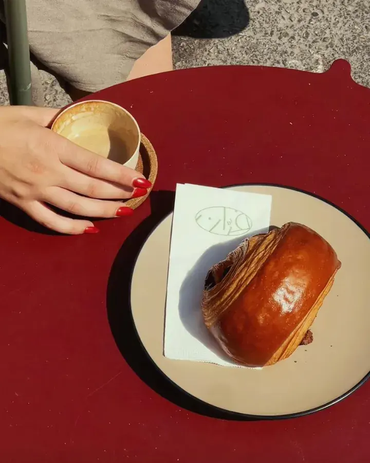 A glazed pastry on a plate next to a cup of coffee on a red café table