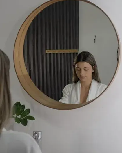A woman in a white robe seen in a round wooden mirror