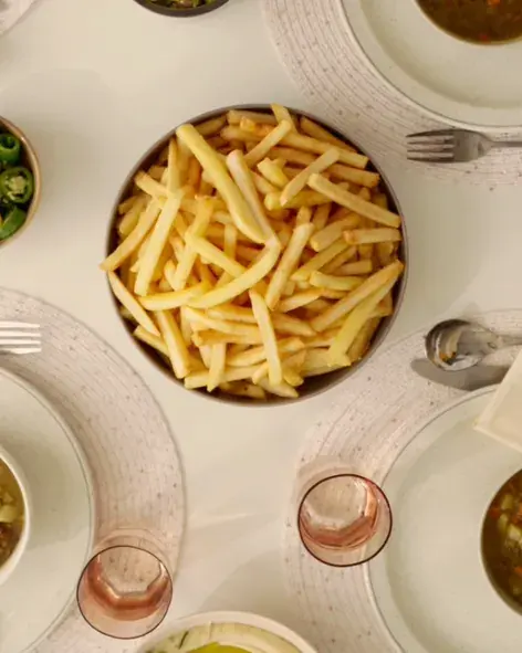 A bowl of fries with side dishes on a white table, seen from above